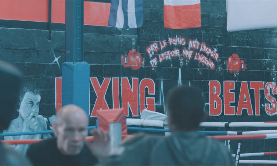 Fresque murale sur un ring de boxe avec l'inscription 'Par le poing naît l'espoir, de l'espoir naît l'histoire' et les mots 'Boxing Beats', vue d'un gymnase de boxe solidaire.