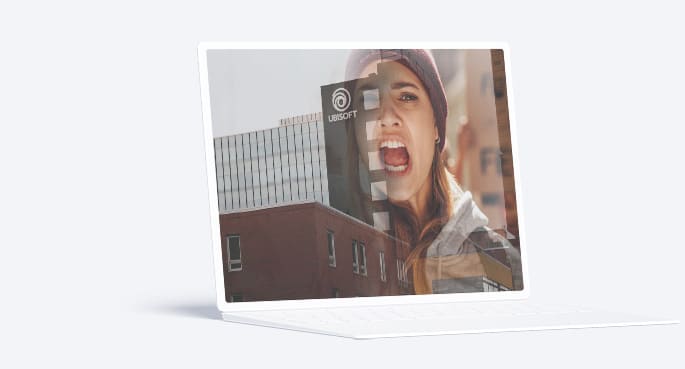 Image d'un ordinateur portable blanc avec une photo sur l'écran montrant une femme manifestant, superposée sur l'image d'un bâtiment qui porte le logo d'Ubisoft. L'effet de superposition donne l'impression que la femme est à la fois devant l'ordinateur et sur le site en arrière-plan. L'ensemble crée un visuel dynamique qui semble exprimer l'énergie et qui valorise un message de réclamation ou de protestation.
