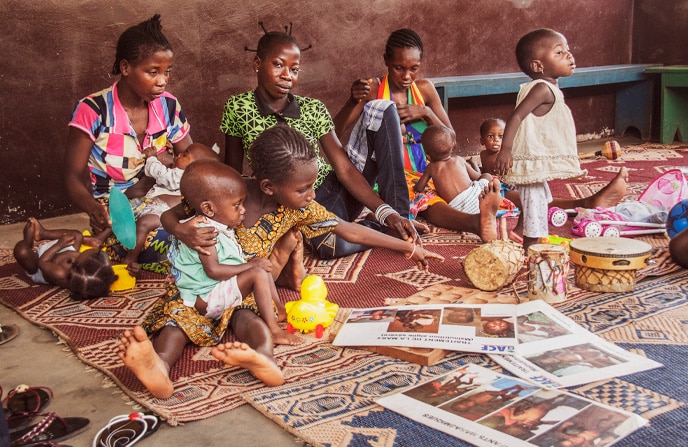 Plusieurs mères centrafricaines et leurs enfants assistant à un atelier de soins psycho-sociologiques à l'hôpital pédiatrique de Bangui. Les enfants jouent et les adultes écoutent, dans un environnement chaleureux, décoré de tapis et de jouets.
