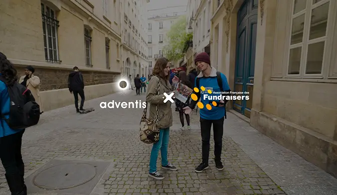 Deux jeunes, un homme et une femme, s'engagent dans une conversation animée dans une rue animée près de bâtiments historiques, où est réalisée une collecte de fonds. Les logos d'Adventis et de l'Association Française des Fundraisers sont visibles au premier plan, illustrant leur partenariat pour la promotion du fundraising.